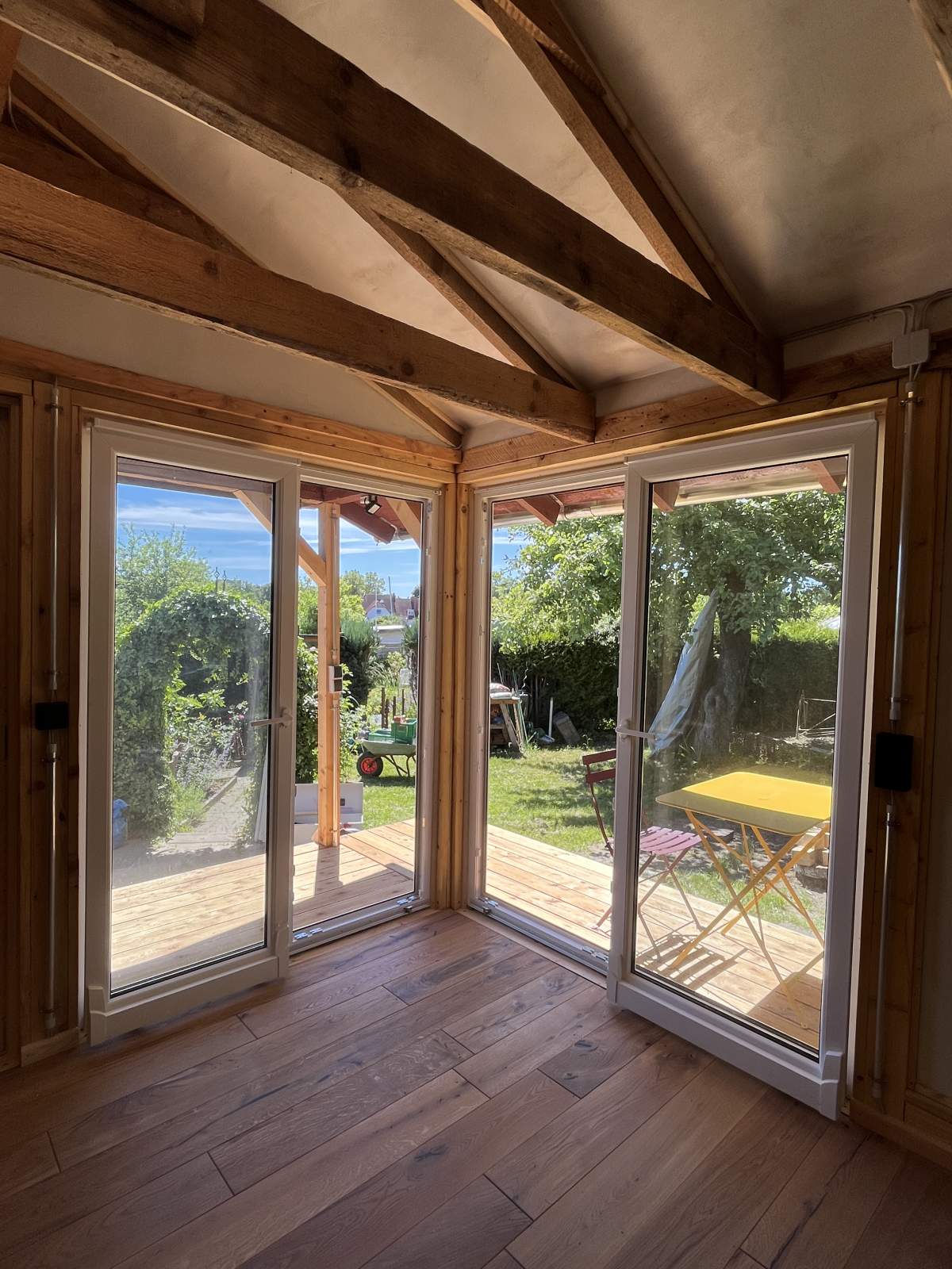 Gartenhaus-Innenraum: Terrassentüren mit Blick in den Garten, offene Balkenkonstruktion