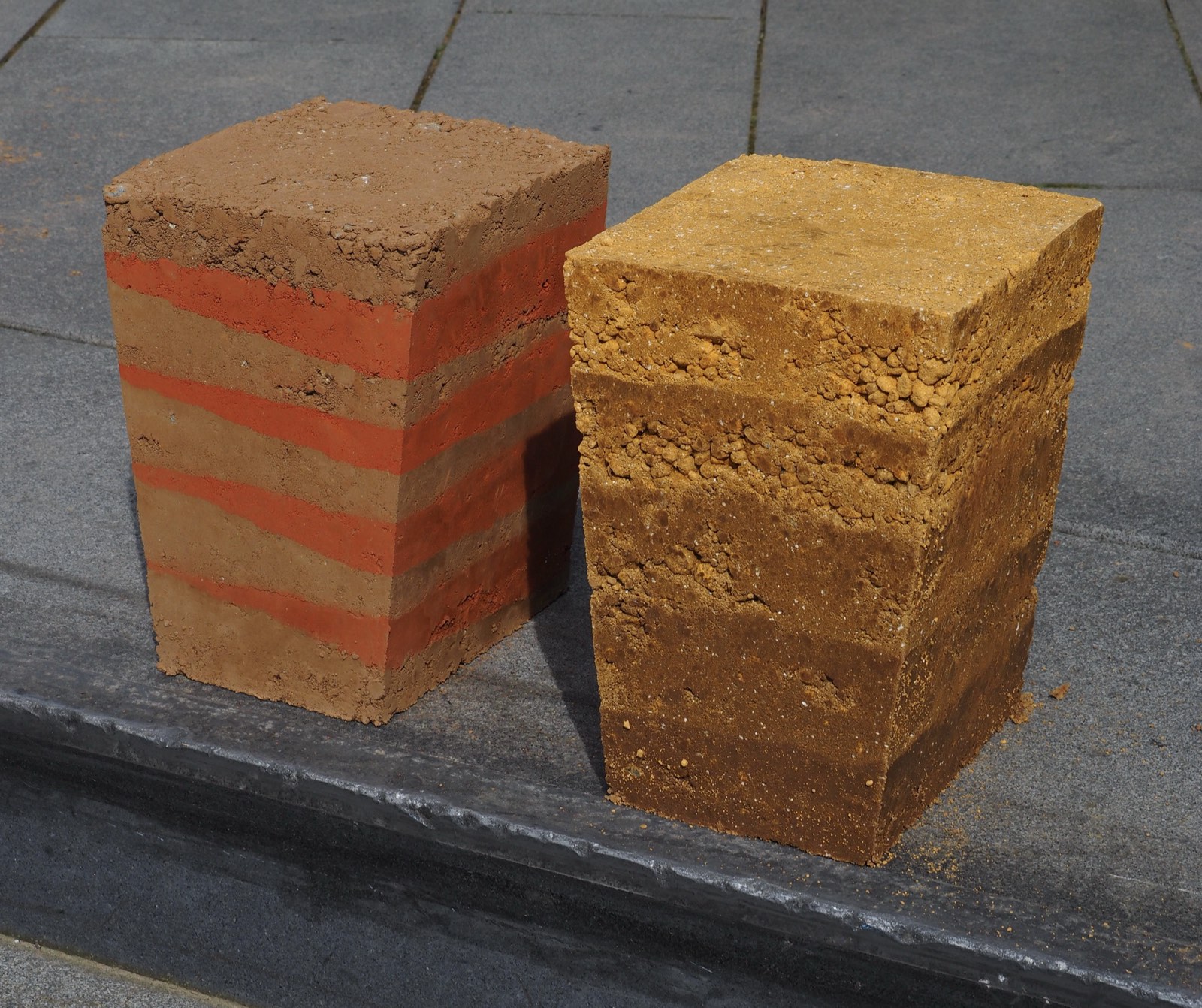 Stampflehm-Workshop: zwei Lehmziegelproben mit Schichtstruktur, rot-beige Lagen