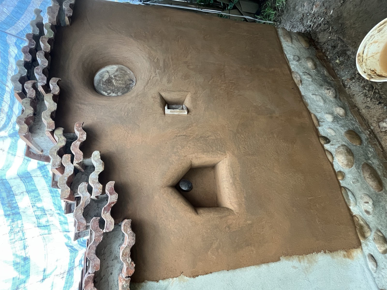 Lehmwand mit eingearbeiteten geometrischen Öffnungen und Wandnischen, Dachziegelabdeckung